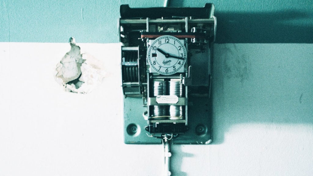 Vintage mechanical punch clock mounted on a wall with exposed gears and wiring