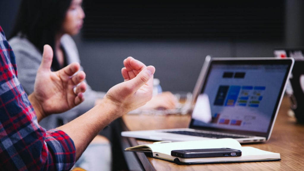 Manager speaking openly and truthfully with employees during a meeting, with laptop and notes on the table.