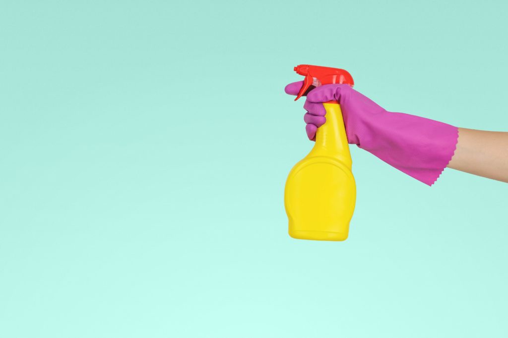 Hand in a pink rubber cleaning glove holding a bottle of cleaner